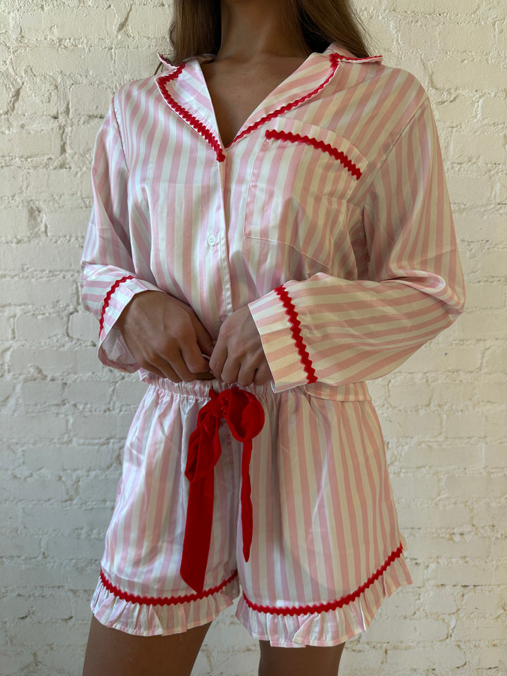Woman wearing light pink and white striped pajamas with red trim and red Merry and Bright wording on the back. 