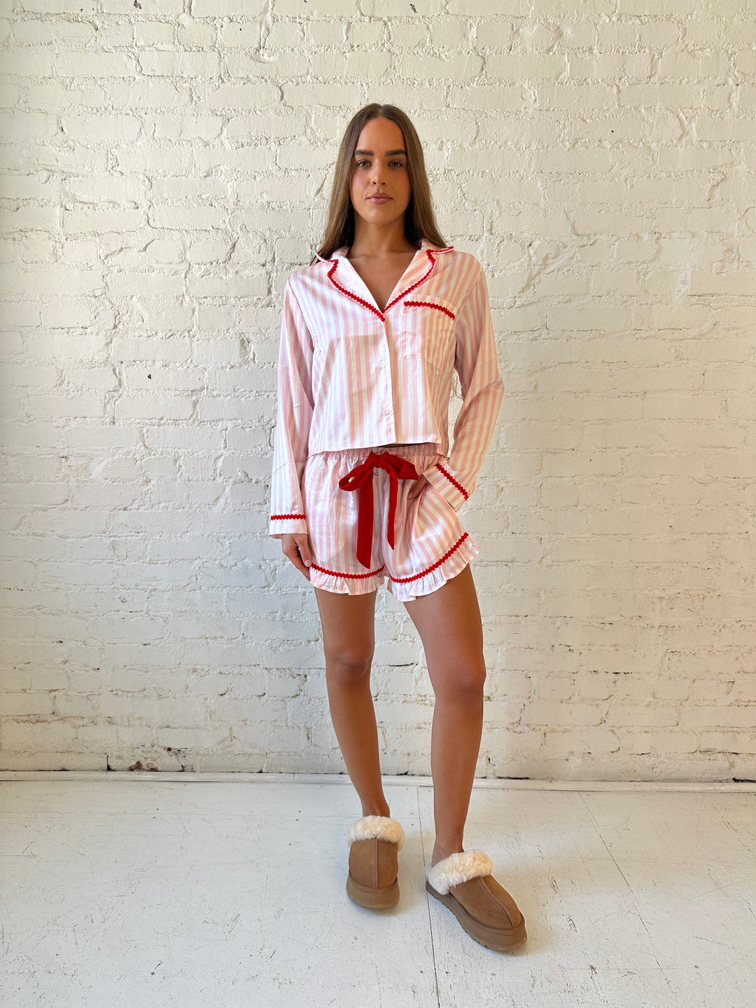 Woman wearing light pink and white striped pajamas with red trim and red Merry and Bright wording on the back. 