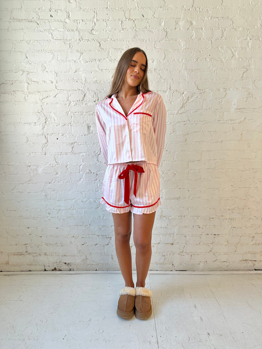 Woman wearing light pink and white striped pajamas with red trim and red Merry and Bright wording on the back. 