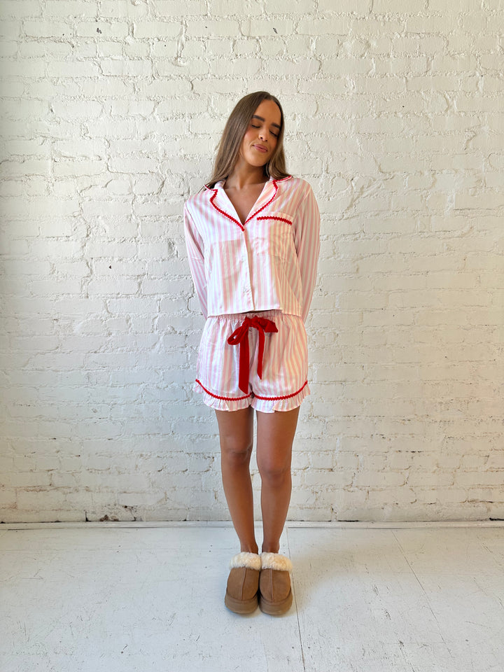 Woman wearing light pink and white striped pajamas with red trim and red Merry and Bright wording on the back. 