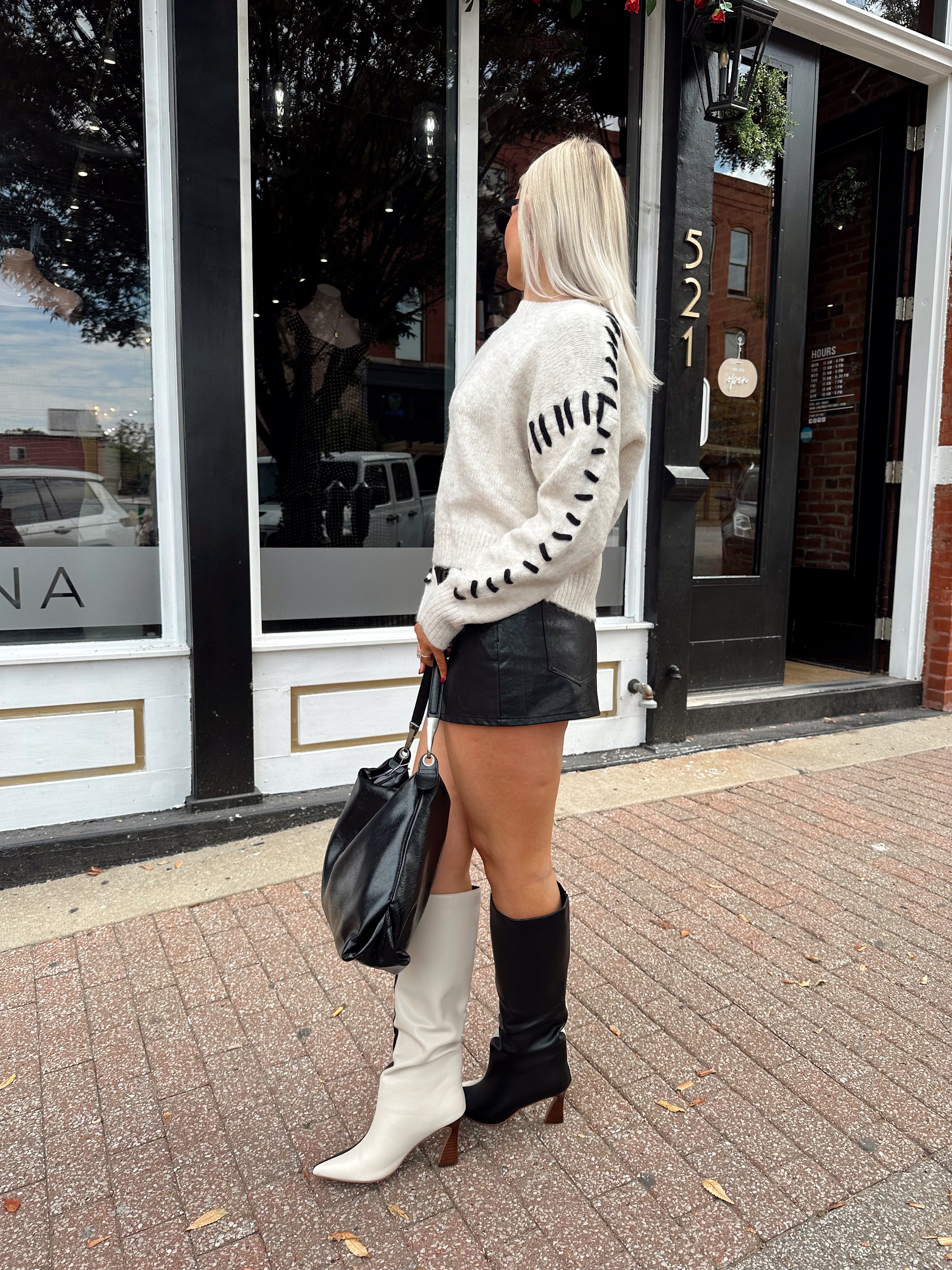 Woman wearing oatmeal knit sweater with black stitch sleeve detailing. 