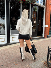 Woman wearing oatmeal knit sweater with black stitch sleeve detailing. 