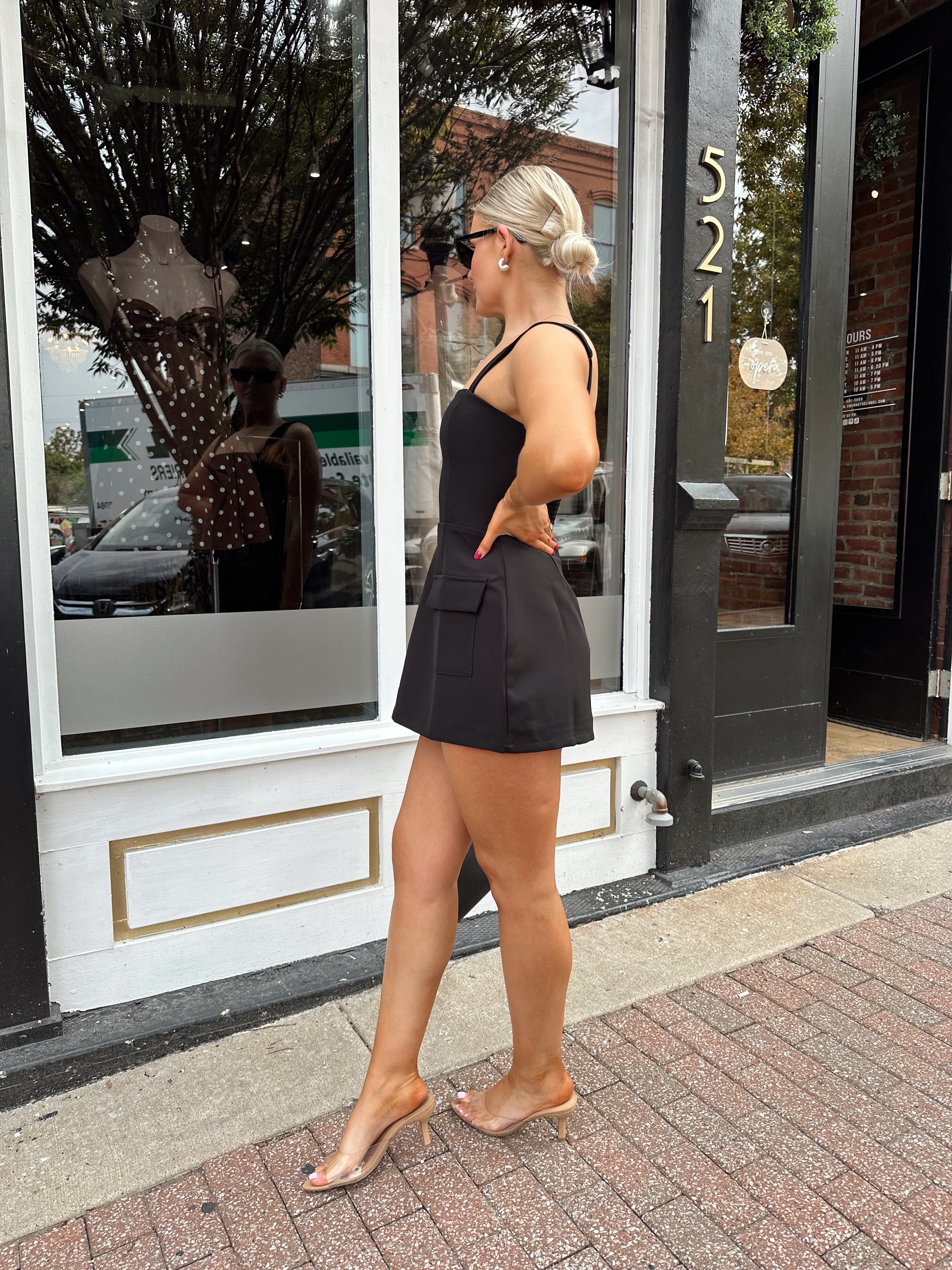 Woman wearing black tailored mini dress with adjustable straps and built in shorts.