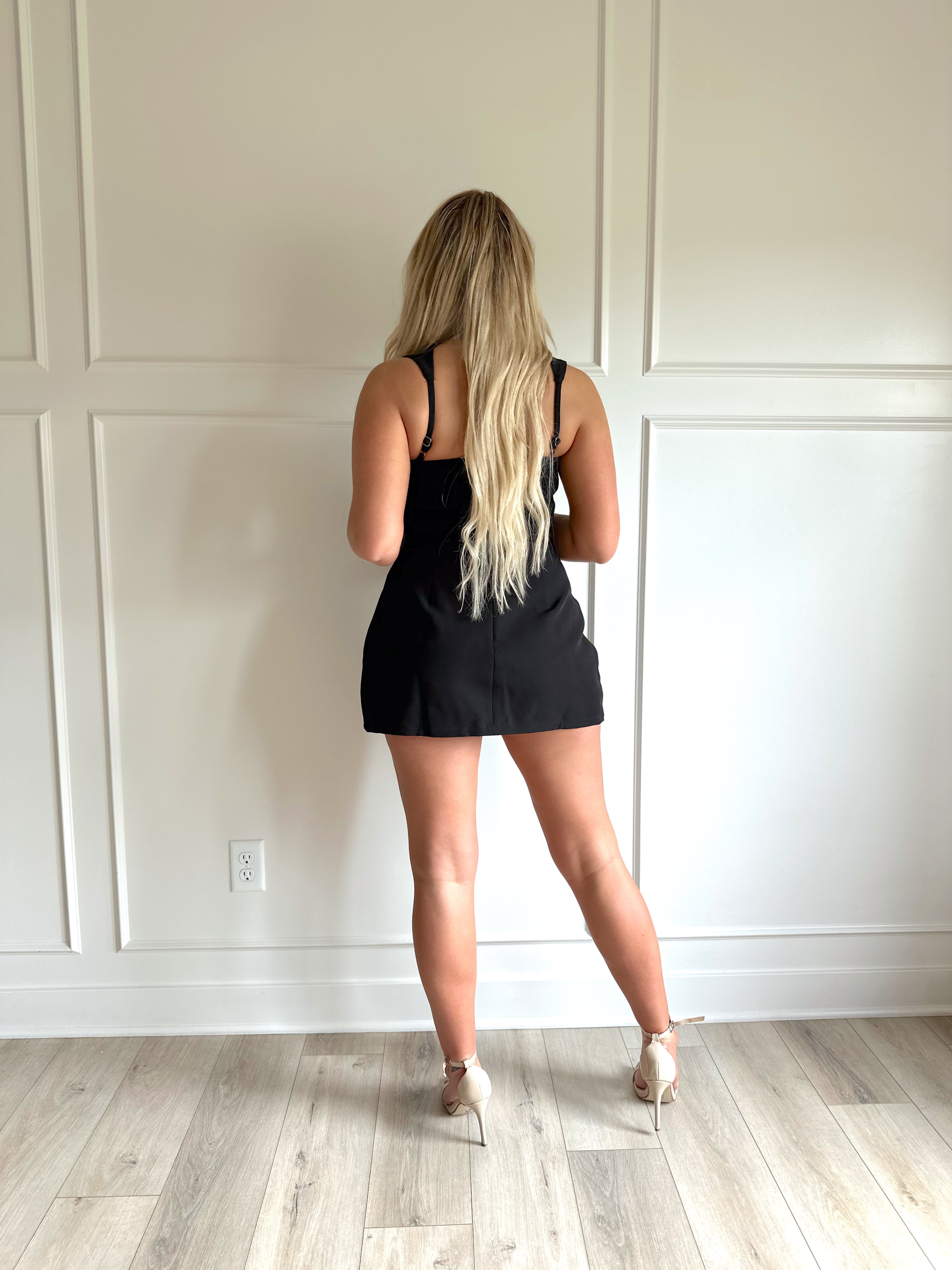 Woman wearing a black tailored mini dress with pocket flaps and built in shorts. 