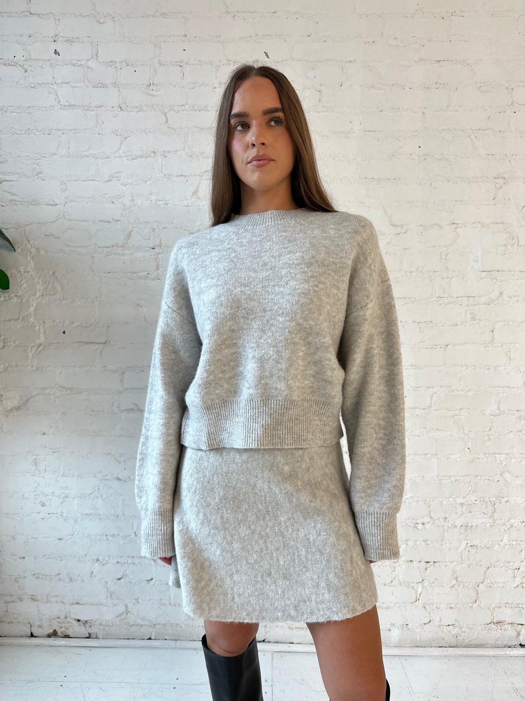 Woman wearing oatmeal colored knit sweater set with long sleeve top and mini skirt bottom.