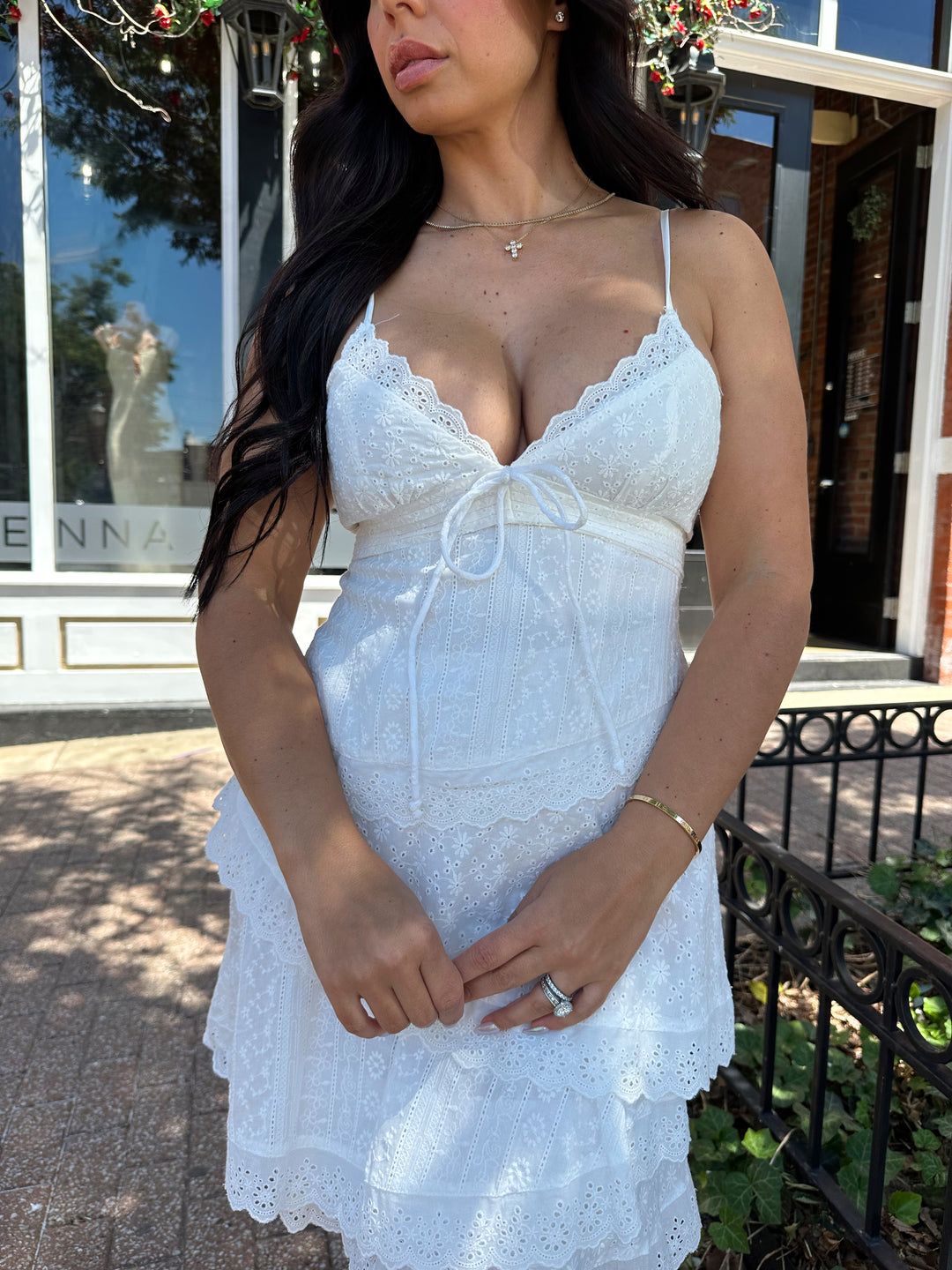 Woman wearing white lace tiered mini dress with adjustable spaghetti straps and tie detail. 