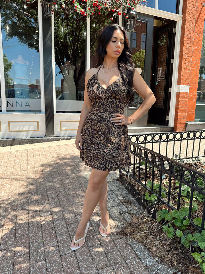 Woman wearing cheetah print mini dress with adjustable straps and ruffle neckline. 