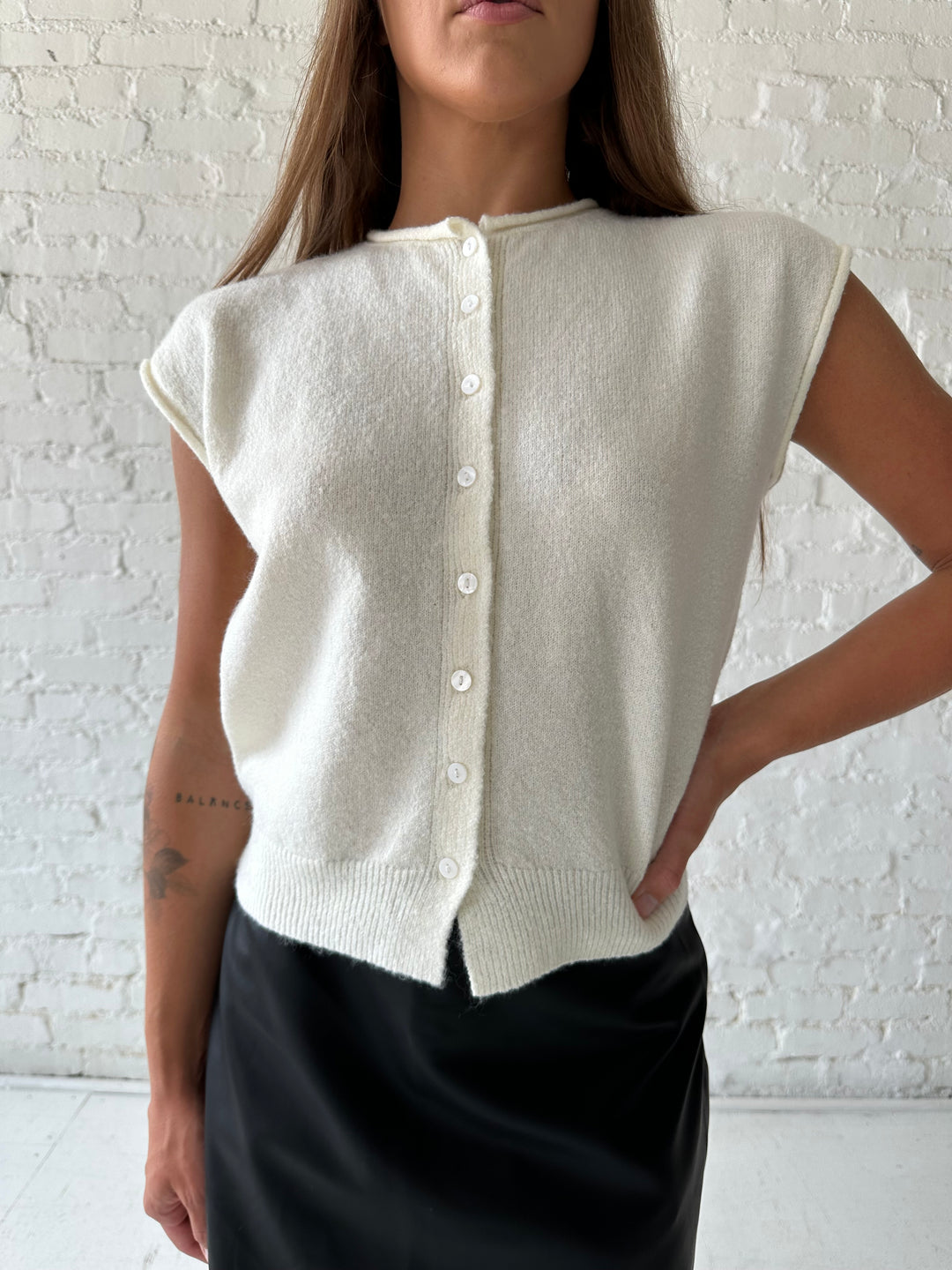 Woman wearing ivory knit button down cardigan with black leather skort. 