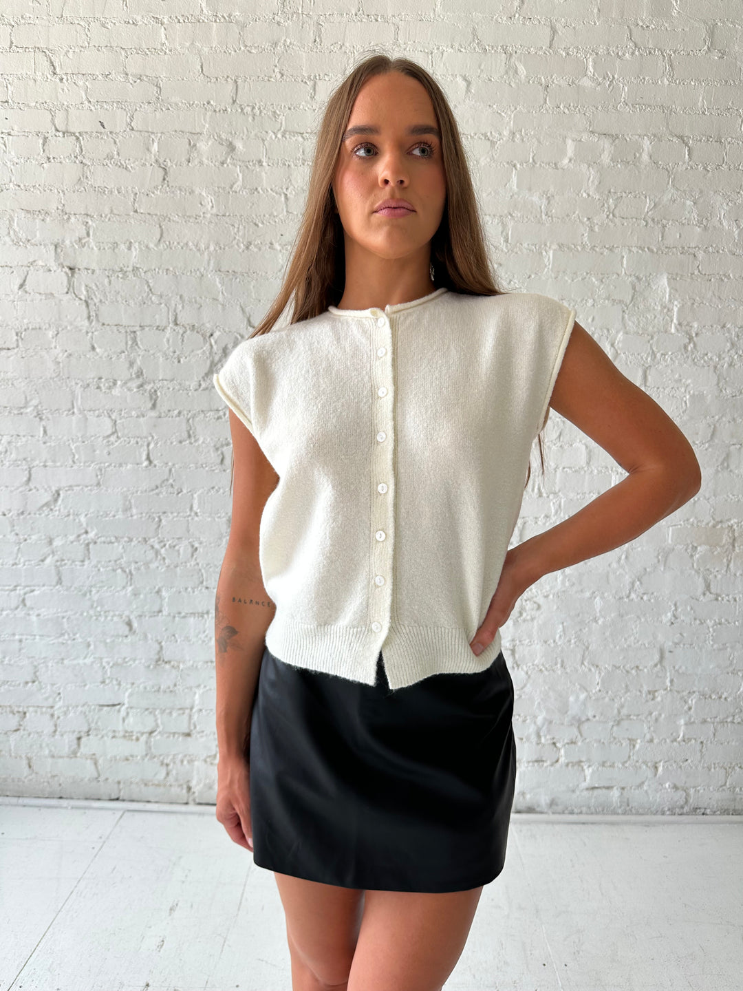 Woman wearing ivory knit button down cardigan with black leather skort. 