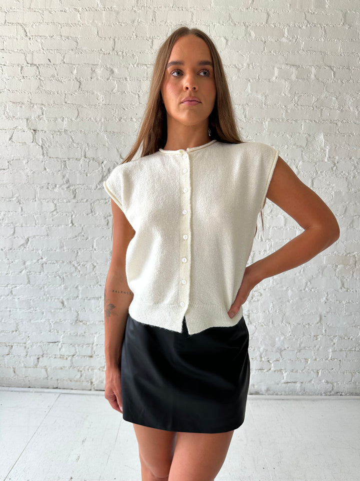 Woman wearing ivory knit button down cardigan with black leather skort. 