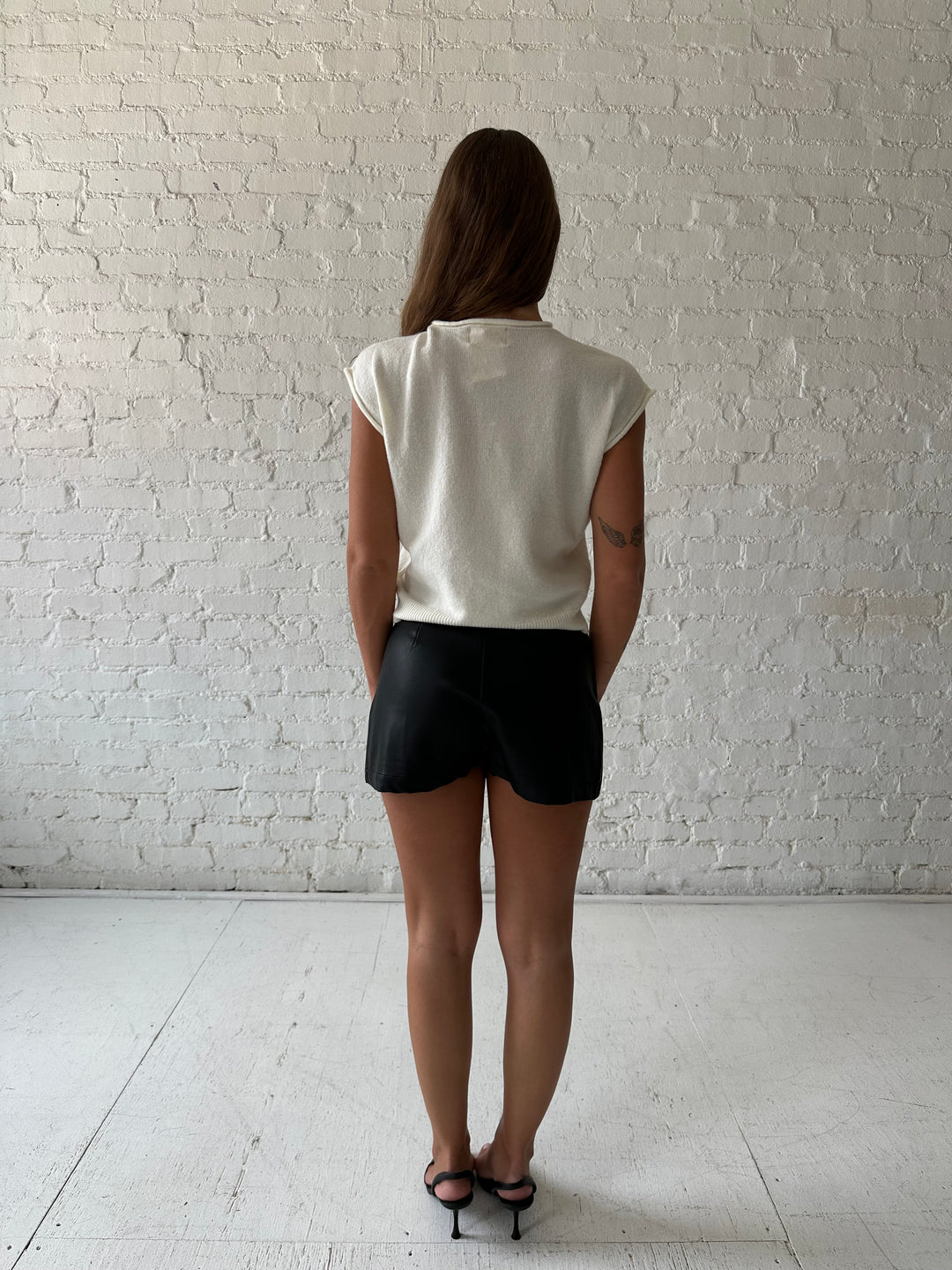 Woman wearing ivory knit button down cardigan with black leather skort. 