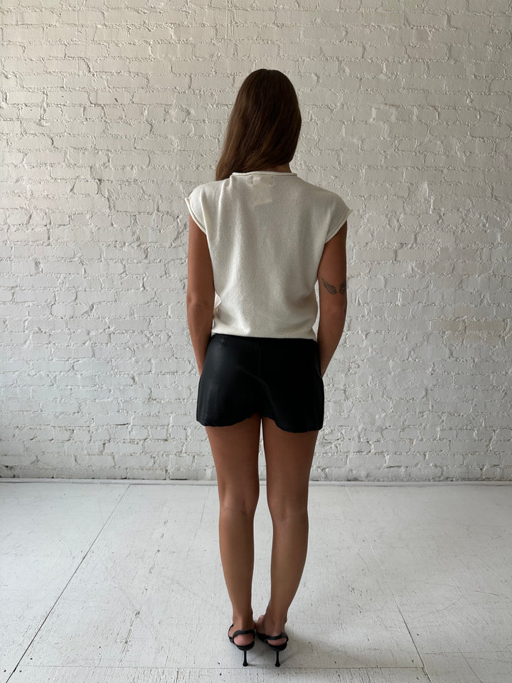 Woman wearing ivory knit button down cardigan with black leather skort. 