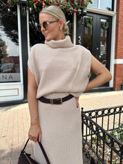 Woman wearing a beige knit two piece sweater set with midi skirt and belt.