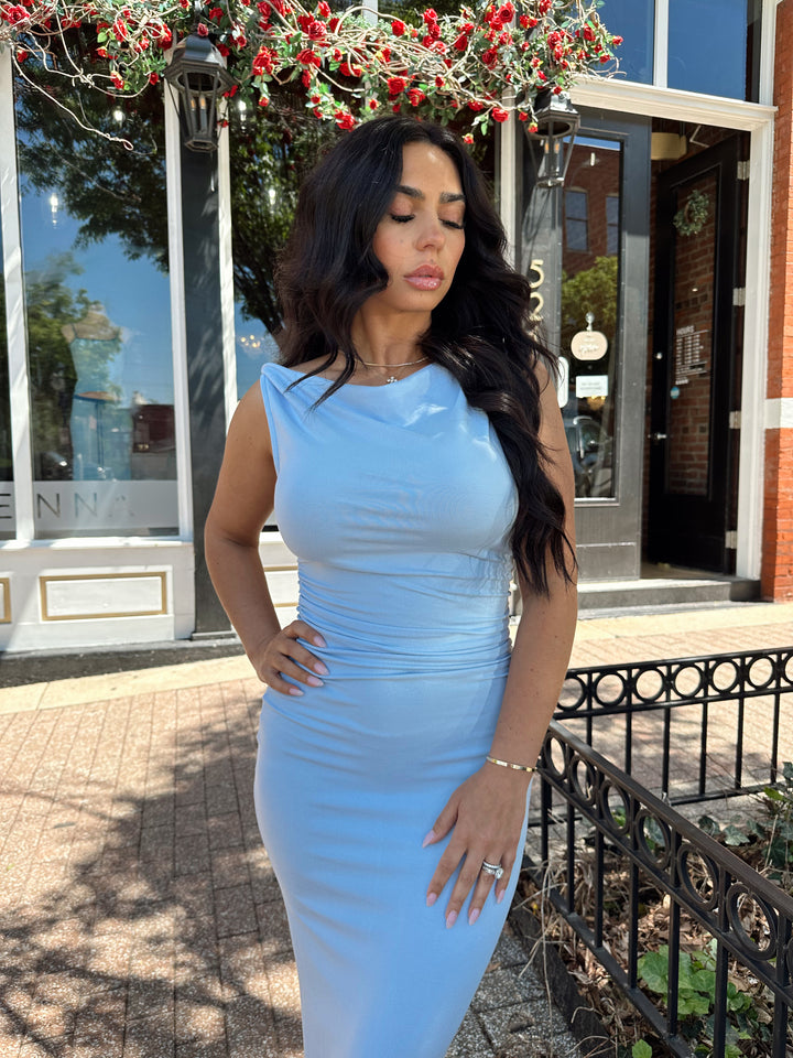 Woman wearing light blue asymmetrical maxi dress with back slit. 