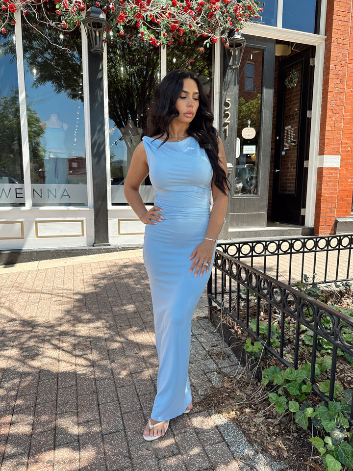 Woman wearing light blue asymmetrical maxi dress with back slit. 
