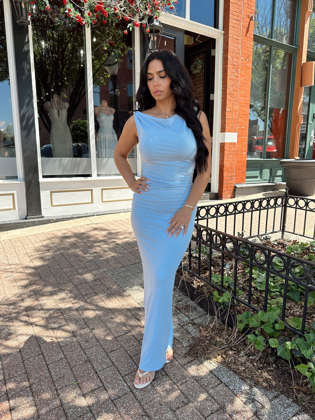Woman wearing light blue asymmetrical maxi dress with back slit. 