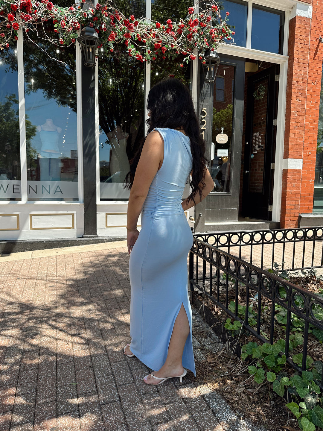 Woman wearing light blue asymmetrical maxi dress with back slit. 