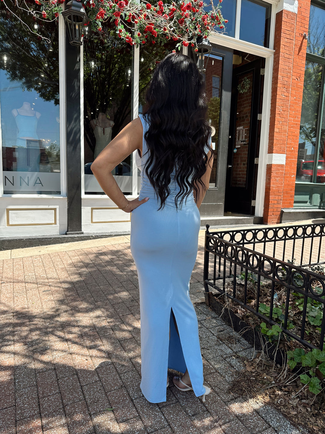 Woman wearing light blue asymmetrical maxi dress with back slit. 