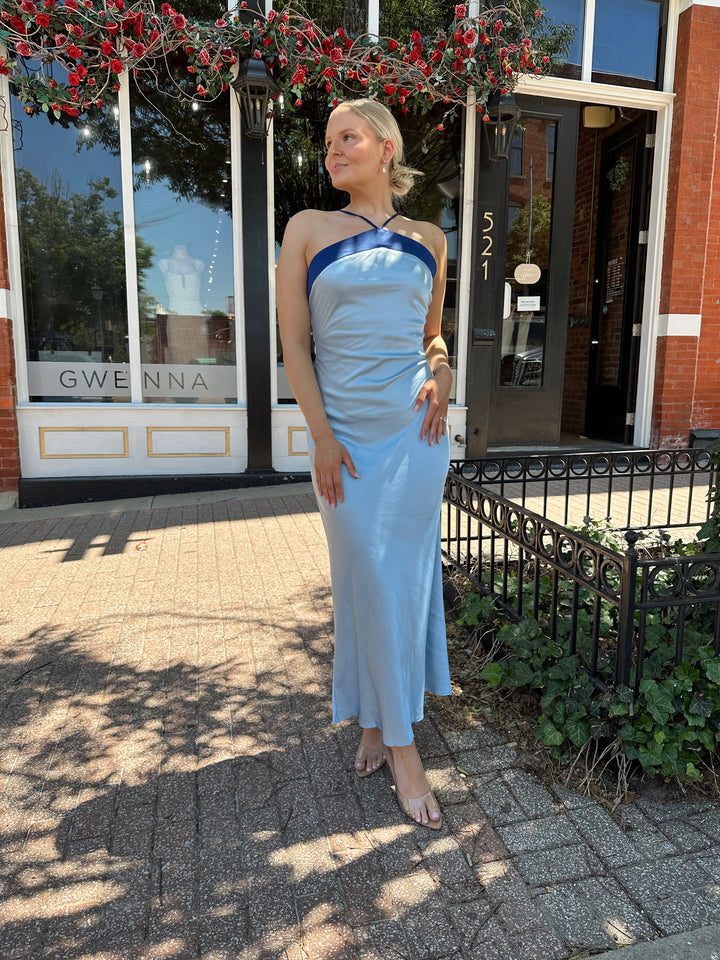 Woman wearing a blue two toned satin maxi dress with a halter neckline, open back, and adjustable straps. 