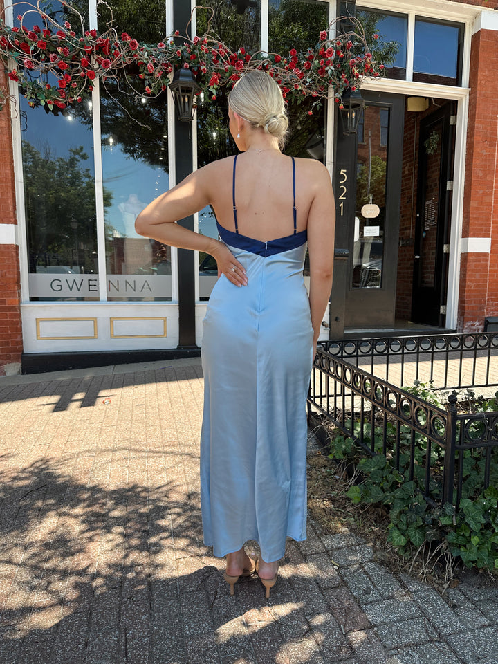 Woman wearing a blue two toned satin maxi dress with a halter neckline, open back, and adjustable straps. 