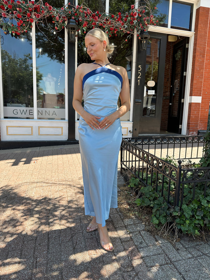 Woman wearing a blue two toned satin maxi dress with a halter neckline, open back, and adjustable straps. 