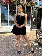 Woman in a black dress standing on a sidewalk with storefronts in the background
