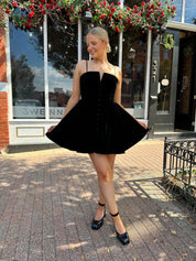 Woman in a black dress standing on a sidewalk with a building in the background
