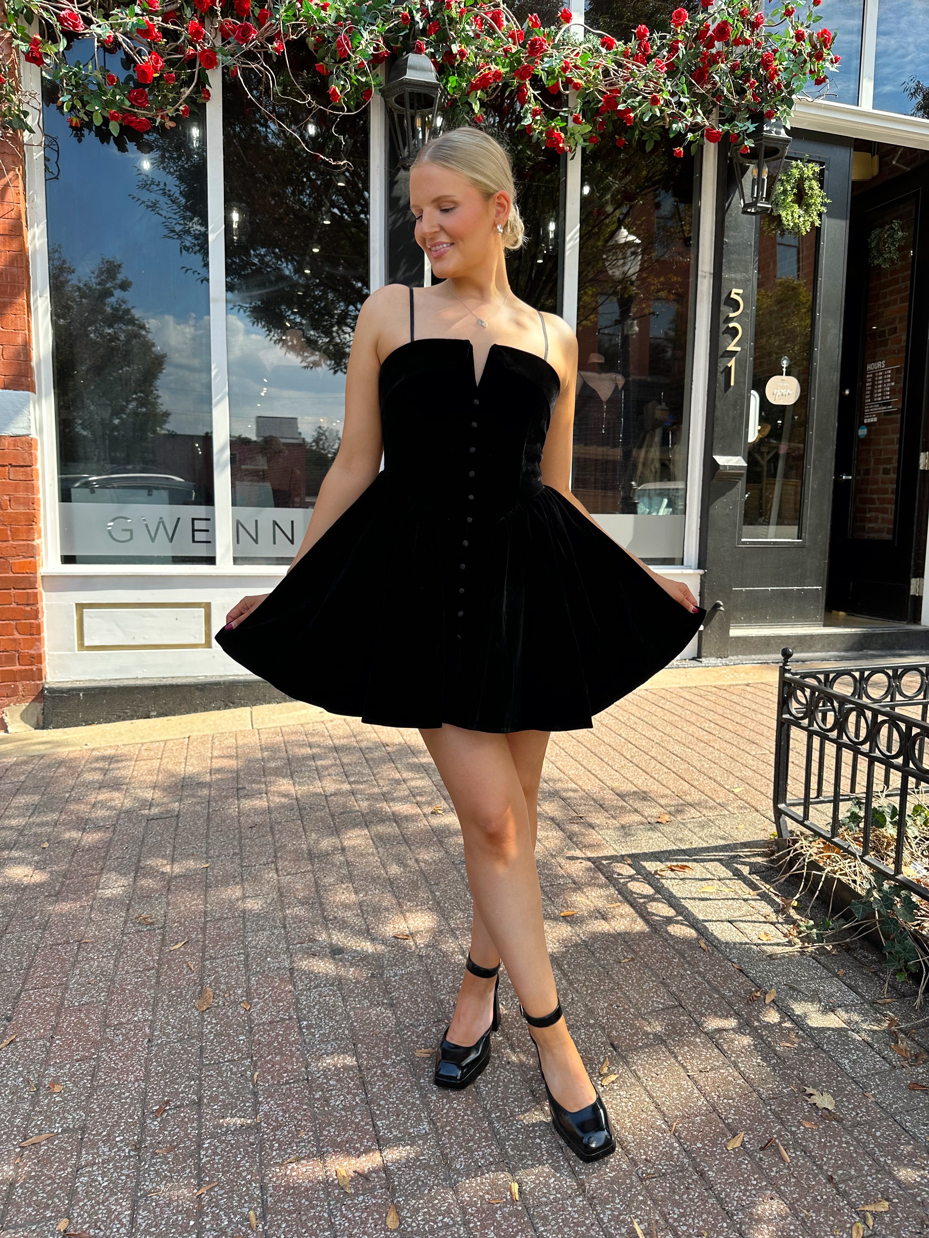 Woman in a black dress standing on a sidewalk with a building in the background