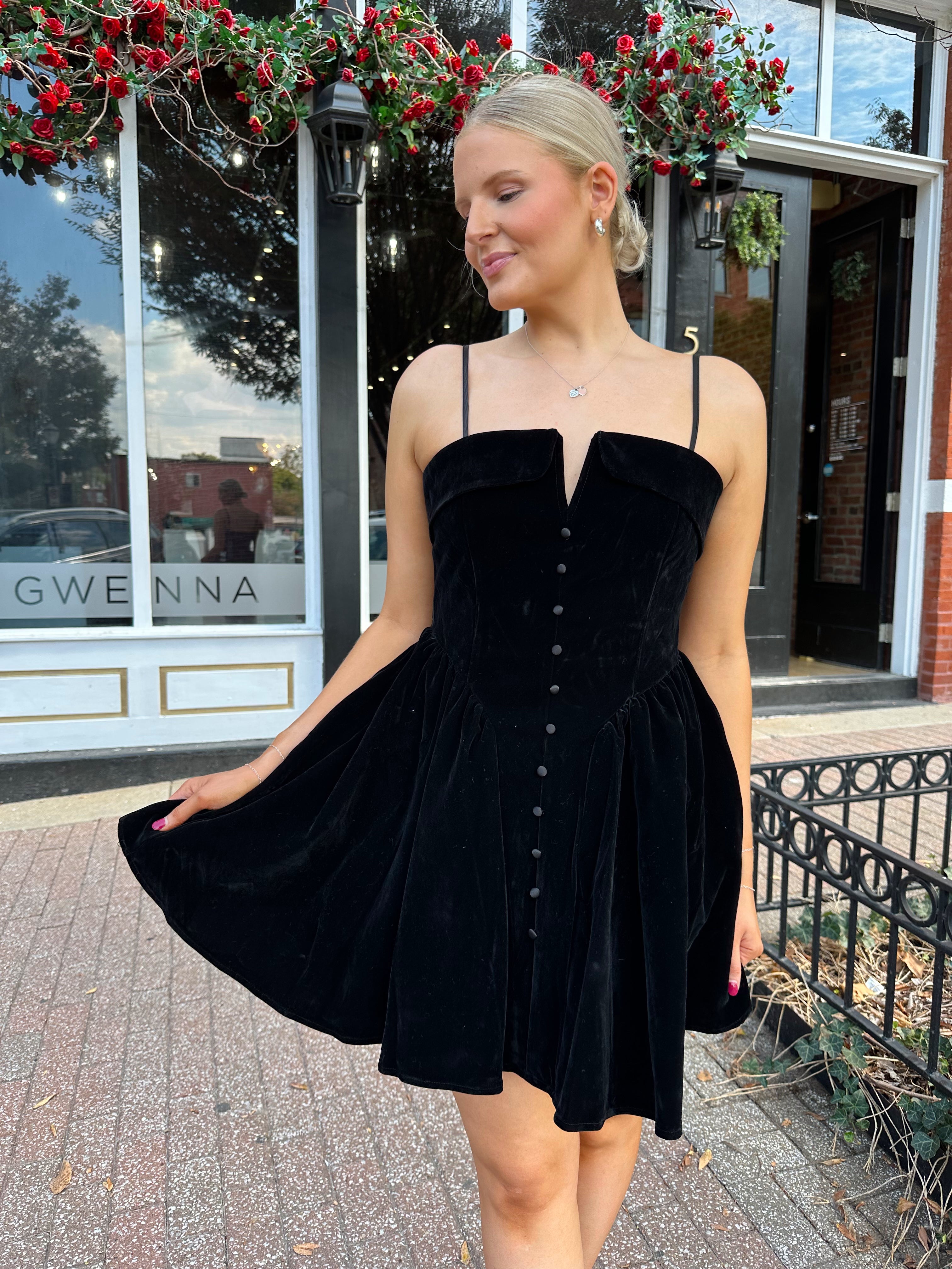Woman in a black dress standing on a street with a building in the background