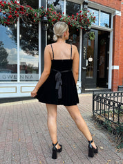 Woman in a black dress standing on a sidewalk in front of a building with decorative elements.