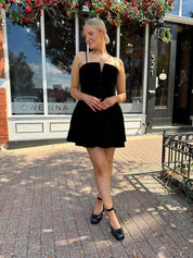 Woman in a black dress standing on a sidewalk in front of a building with a sign that reads 'Gwen'.