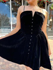 Black velvet dress with button details on a mannequin against a city street background.
