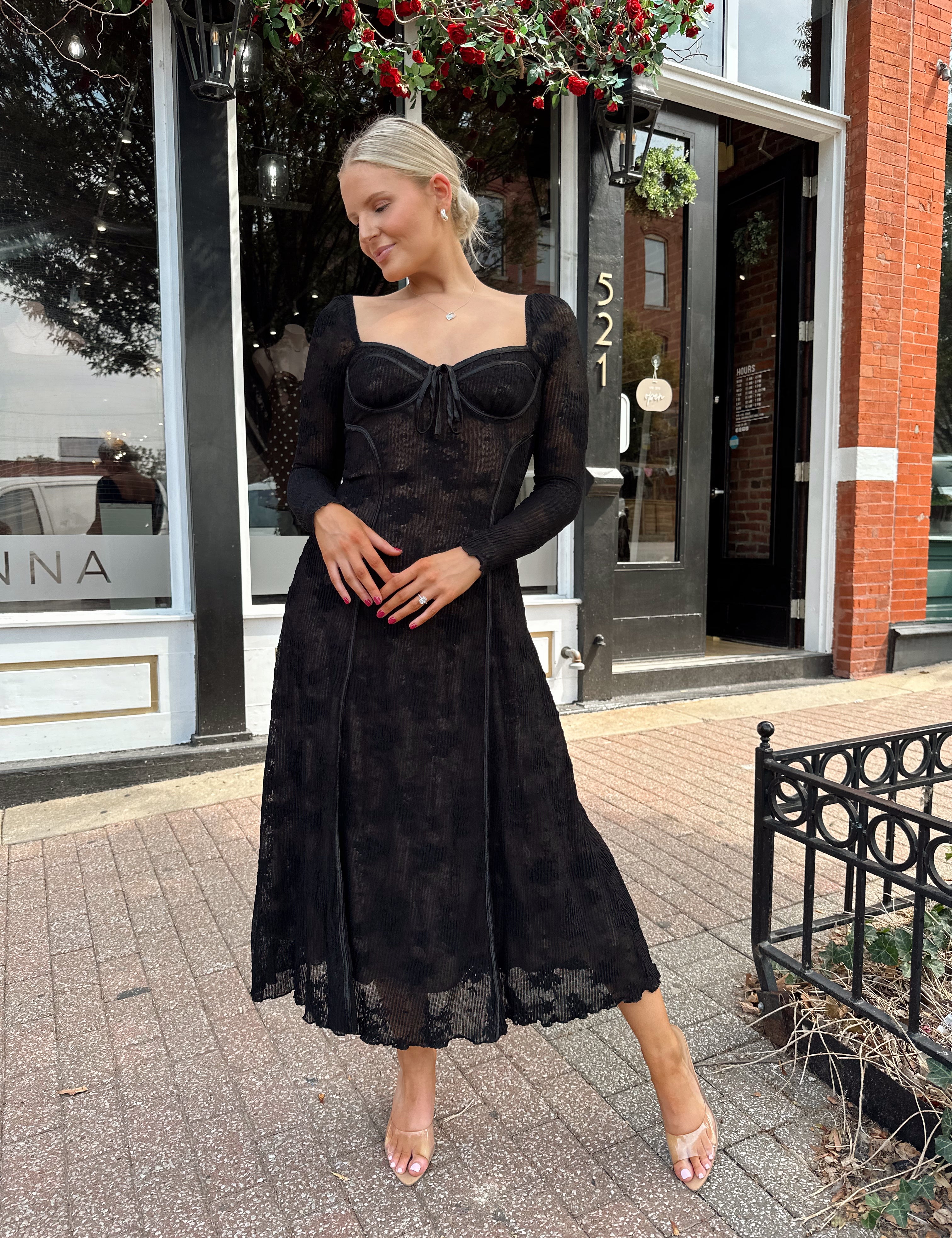 Woman wearing long sleeve black lace midi dress with tan underlay. 