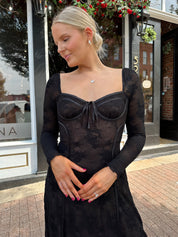 Woman wearing long sleeve black lace midi dress with tan underlay. 