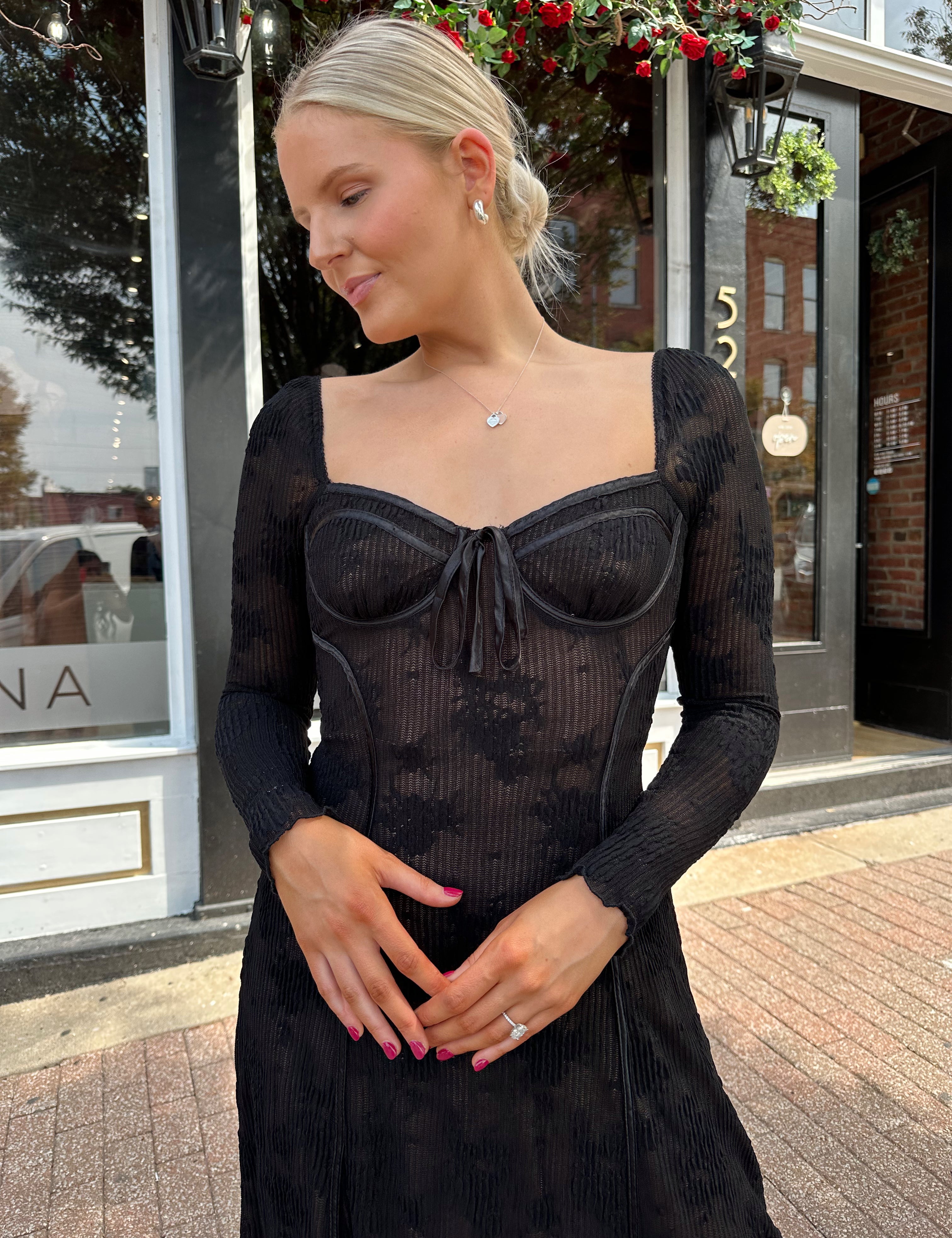 Woman wearing long sleeve black lace midi dress with tan underlay. 