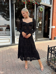 Woman wearing long sleeve black lace midi dress with tan underlay. 