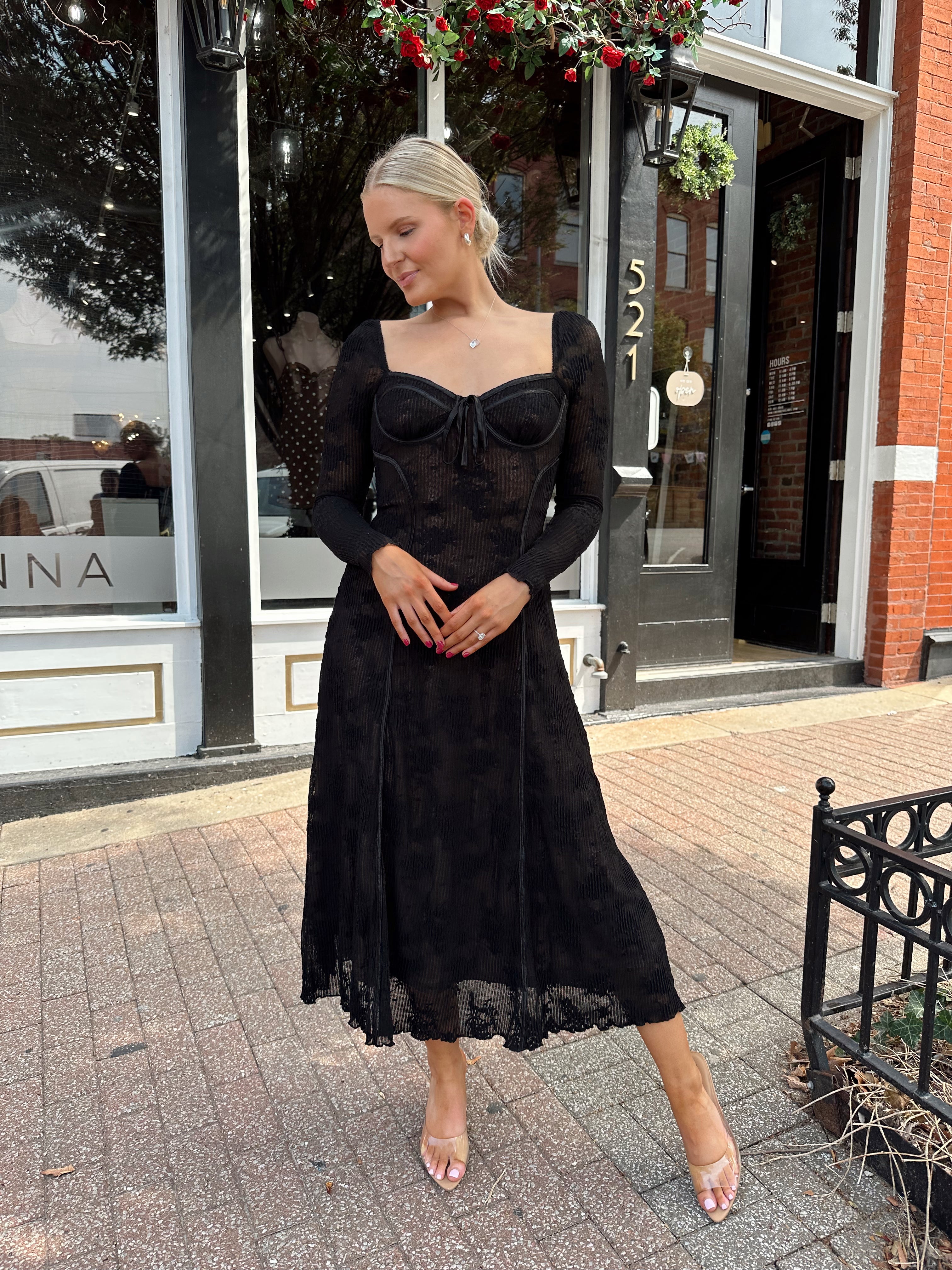 Woman wearing long sleeve black lace midi dress with tan underlay. 