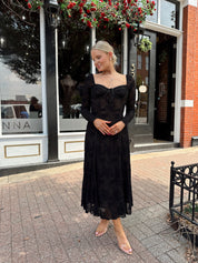 Woman wearing long sleeve black lace midi dress with tan underlay. 