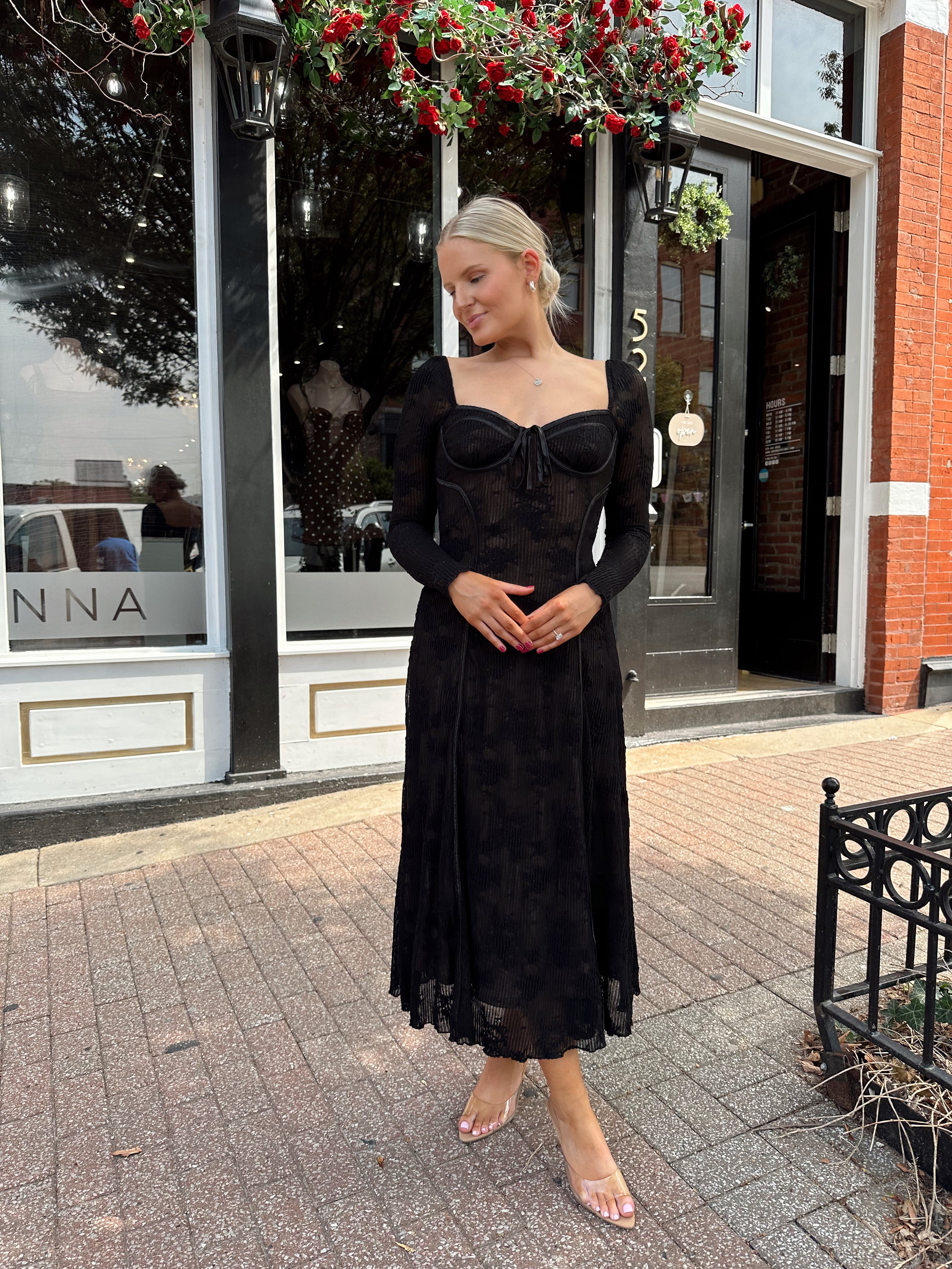 Woman wearing long sleeve black lace midi dress with tan underlay. 
