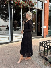 Woman wearing long sleeve black lace midi dress with tan underlay. 