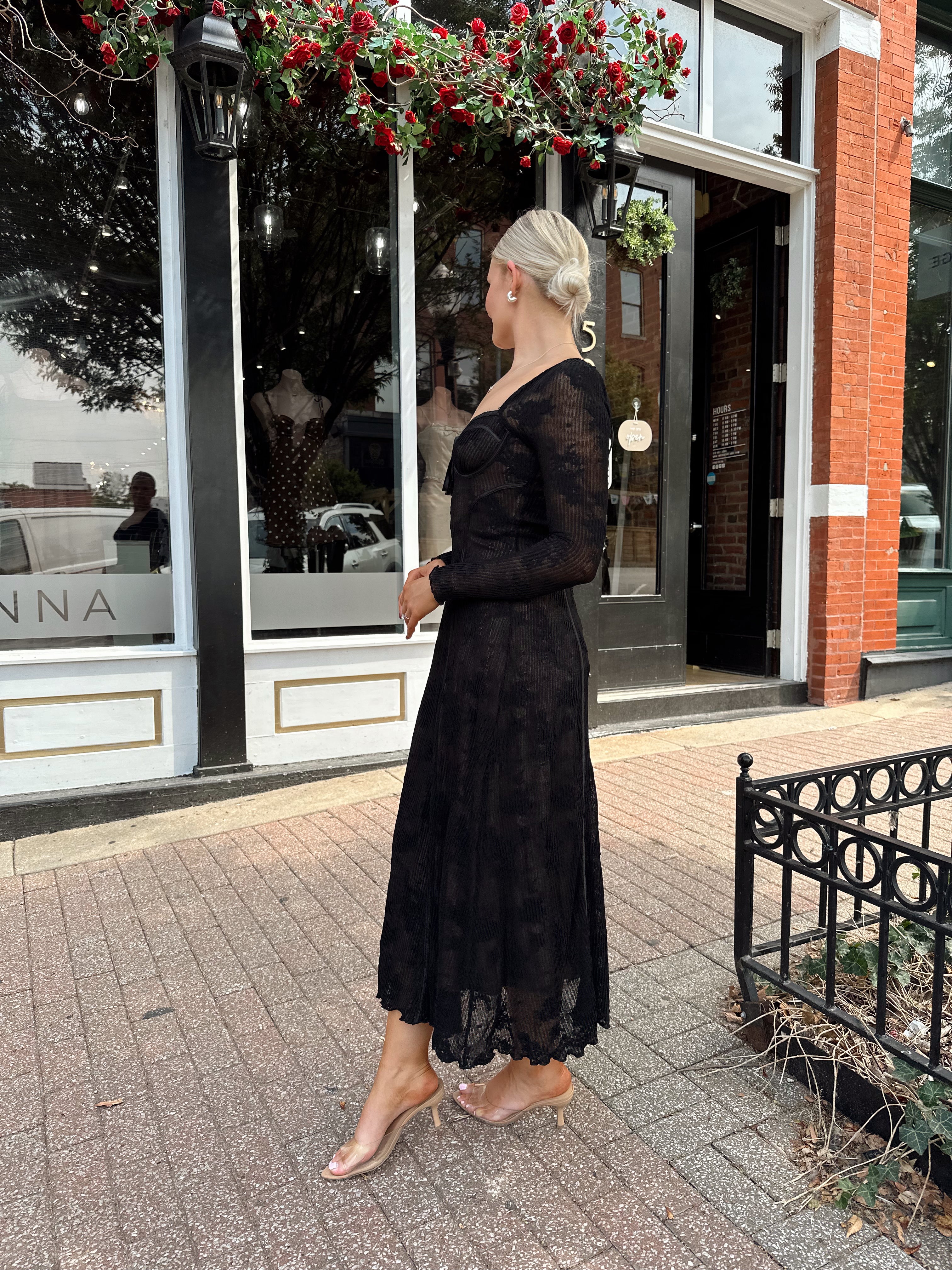 Woman wearing long sleeve black lace midi dress with tan underlay. 