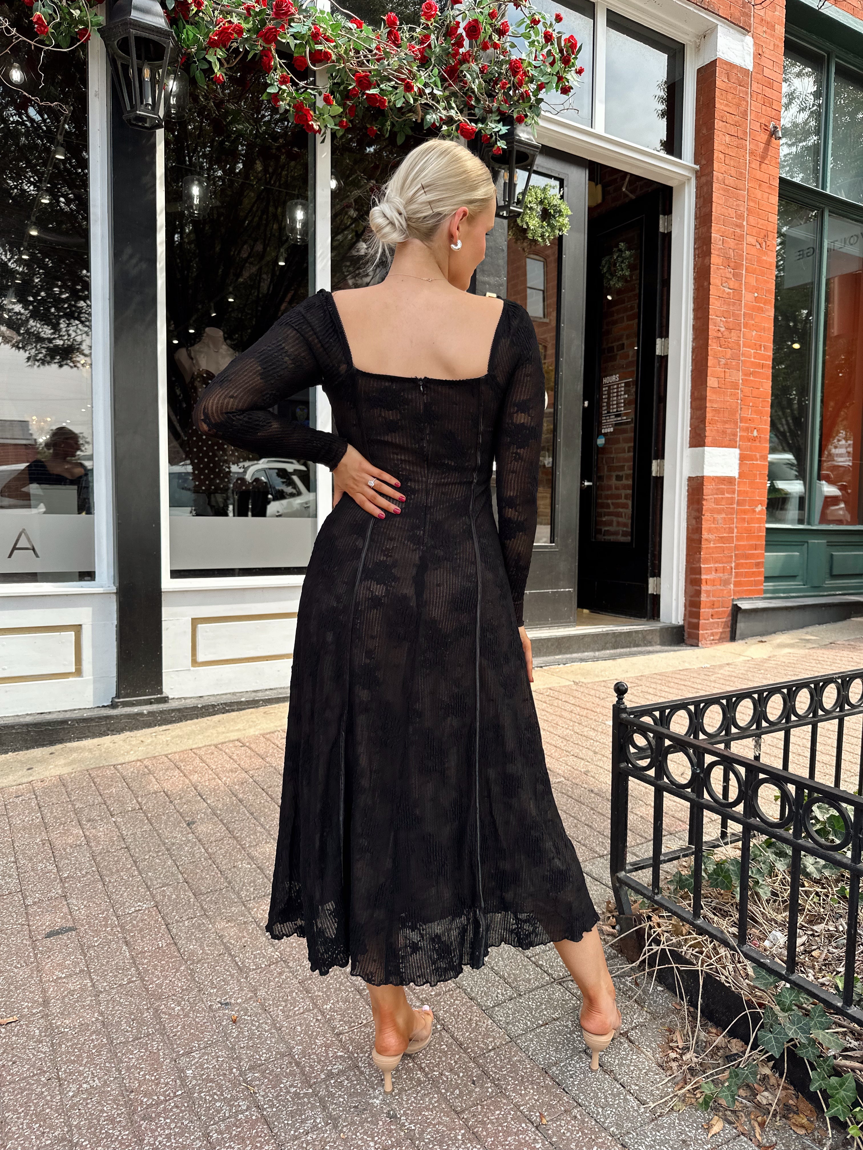 Woman wearing long sleeve black lace midi dress with tan underlay. 