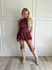 Woman wearing burgundy smocked mini dress with ruffle mini skirt and open back and tie neck.