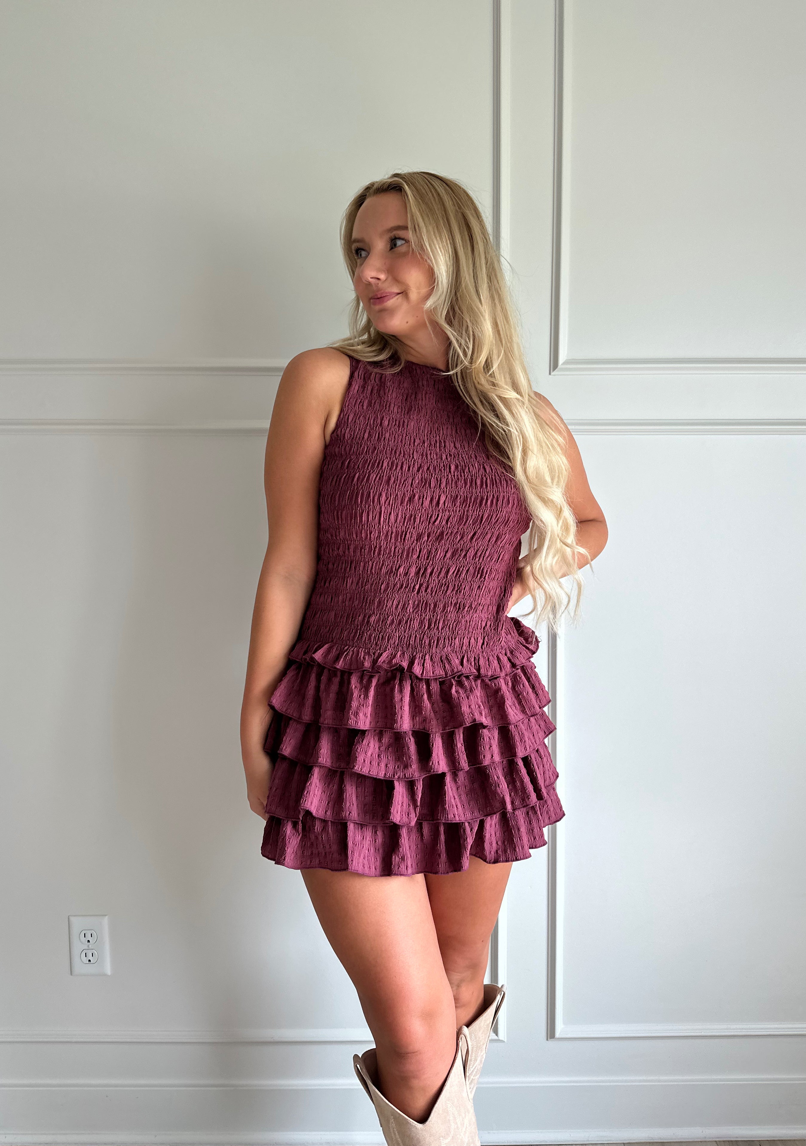 Woman wearing burgundy smocked mini dress with ruffle mini skirt and open back and tie neck.