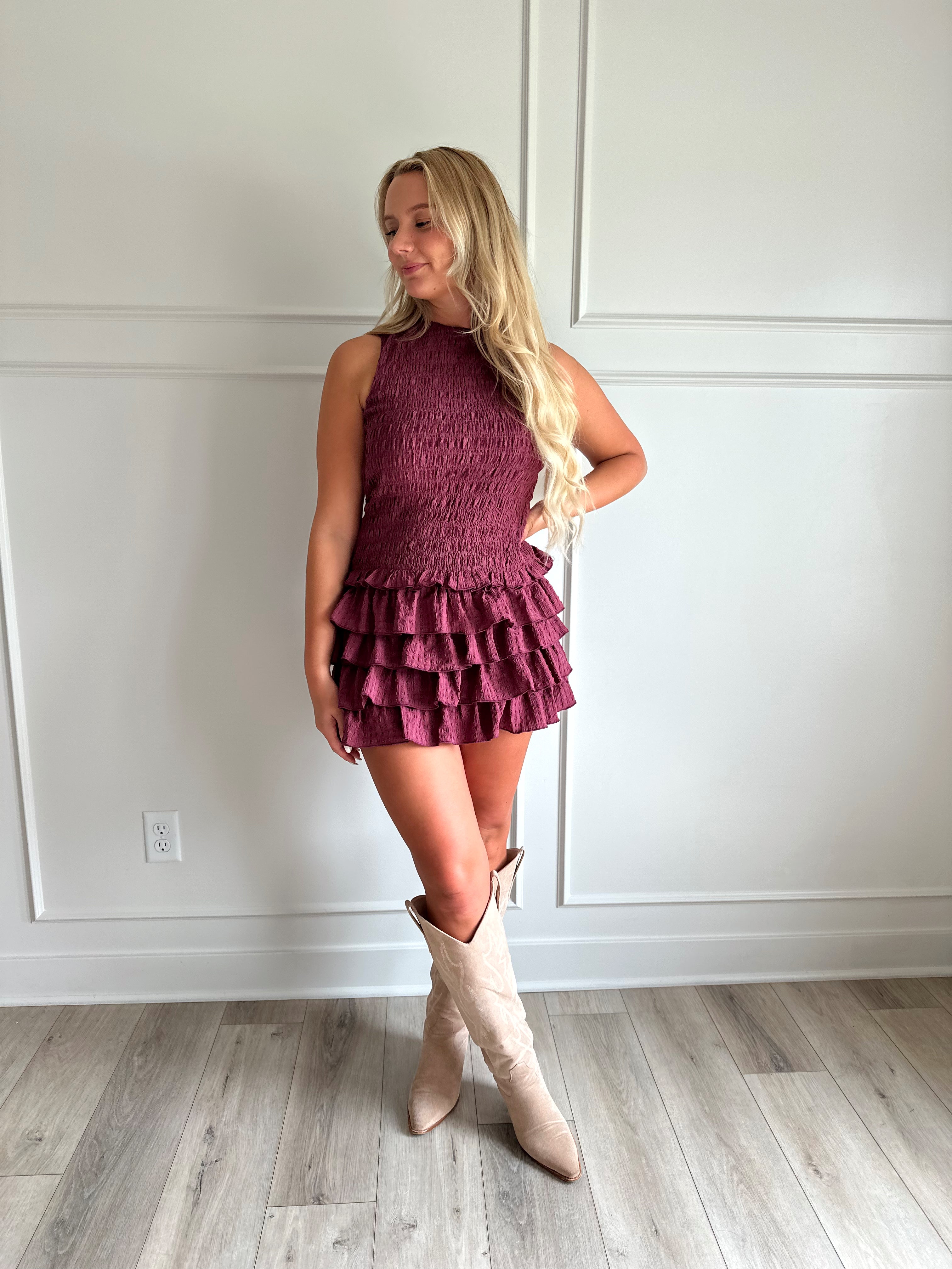 Woman wearing burgundy smocked mini dress with ruffle mini skirt and open back and tie neck.