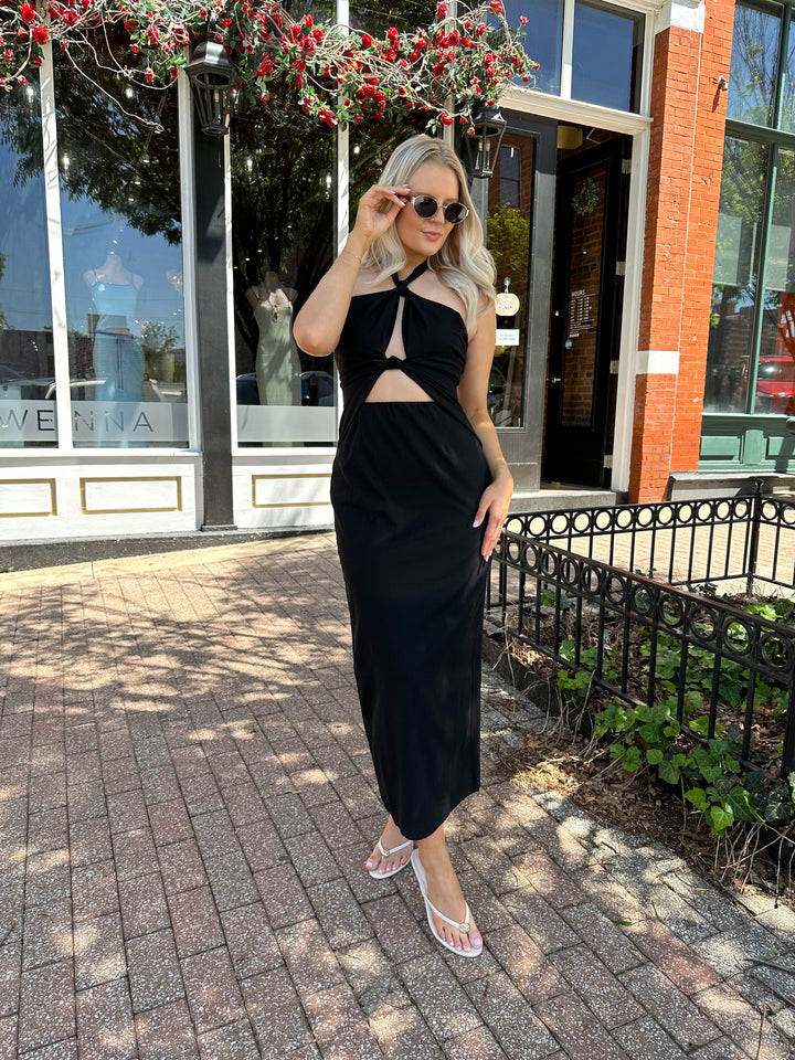 Woman wearing black key hole midi dress with self tie halter and knot detailing. 