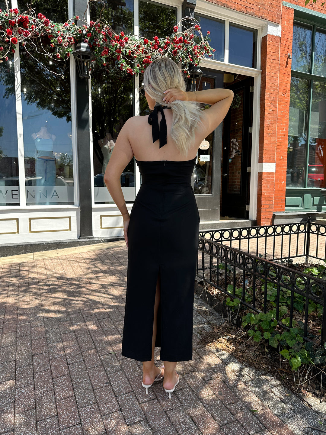 Woman wearing black key hole midi dress with self tie halter and knot detailing. 