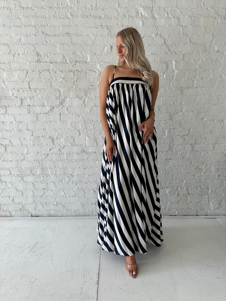Woman wearing navy and white striped maxi dress with straight neckline and adjustable straps. 