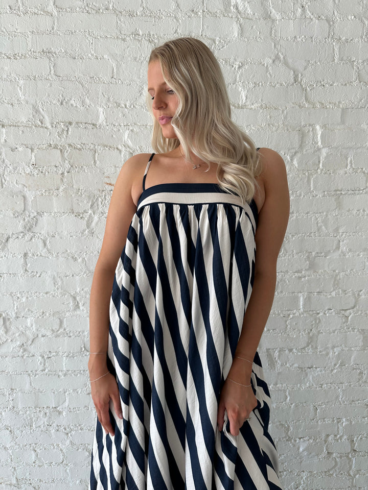 Woman wearing navy and white striped maxi dress with straight neckline and adjustable straps. 