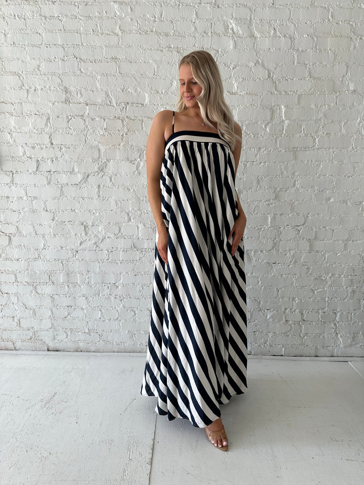 Woman wearing navy and white striped maxi dress with straight neckline and adjustable straps. 